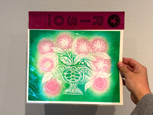 Hand holding a print with a green and pink design against a plain background