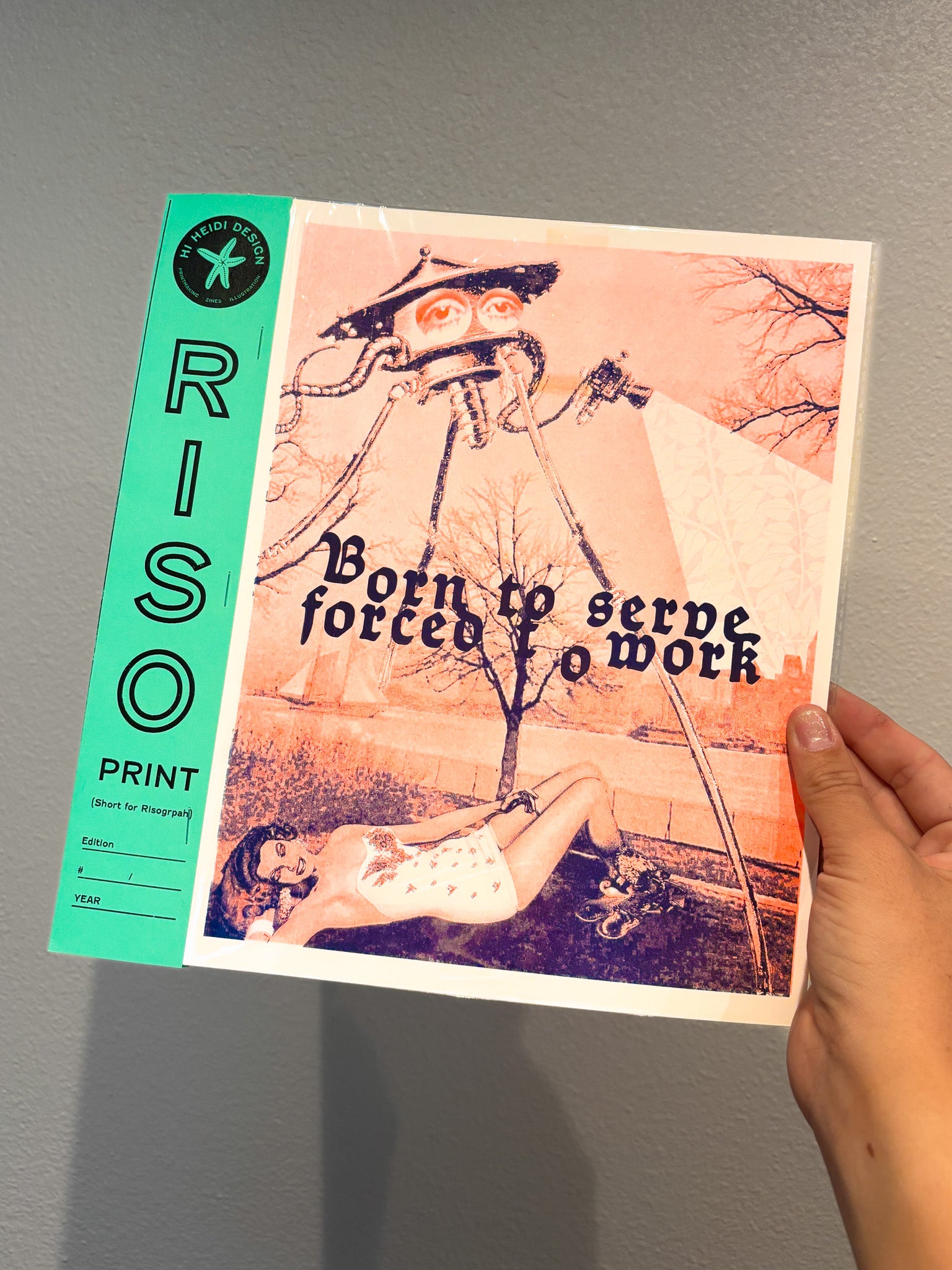 Hand holding a RISO printed book with artistic cover design against a gray background