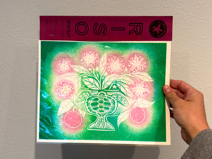 Hand holding a print with a green and pink design against a plain background